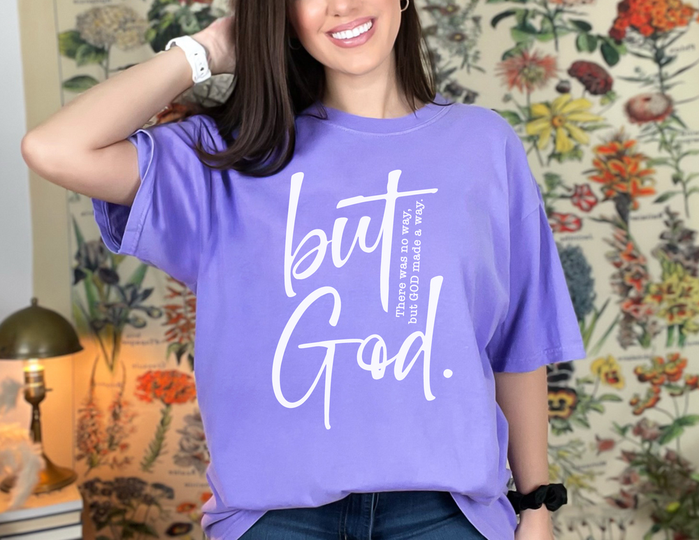 A relaxed fit But God Tee in ring-spun cotton, featuring a woman smiling with her hand on her head. Garment-dyed for coziness, with double-needle stitching for durability. Ideal for daily wear.