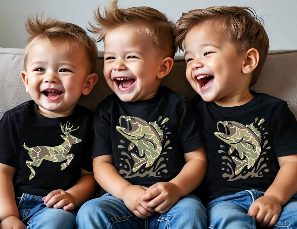 Three toddlers on a couch wear Camo Deer Kids Tees with camouflage animal graphics, laughing and enjoying themselves, showcasing the playful and durable design.