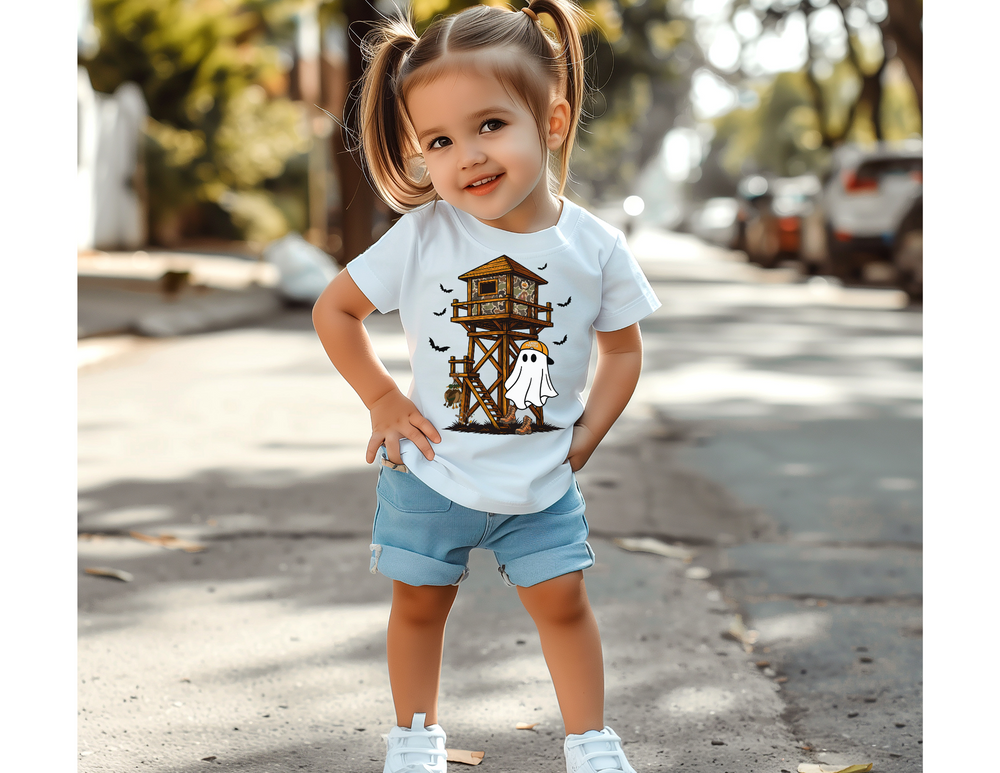 Toddler wearing the Ghost Hunter Kids Tee with a treehouse, bats, and ghost design stands on a sunny street, showcasing the tee's playful graphics and casual style.