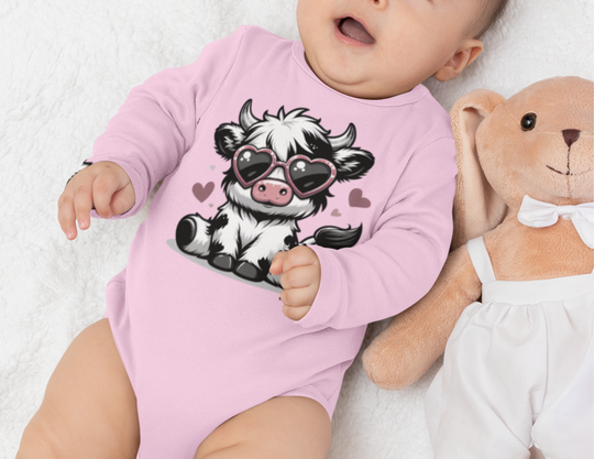 A baby in a Cute Cow Long Sleeve Onesie, lying next to a stuffed animal. Soft, durable 100% cotton fabric with plastic snaps for easy changing. Perfect for infants.