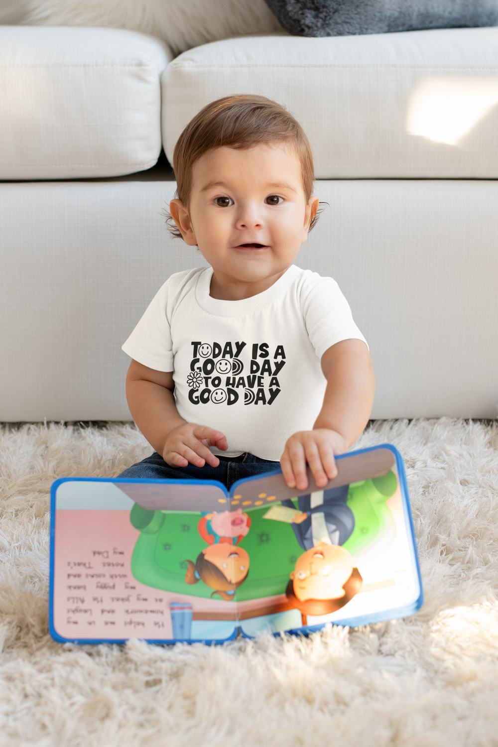A baby in a white shirt sits on the floor reading a book. Good Day to Have a Good Day Onesie: infant fine jersey bodysuit, 100% cotton, ribbed knit bindings, plastic snaps for easy changing access.
