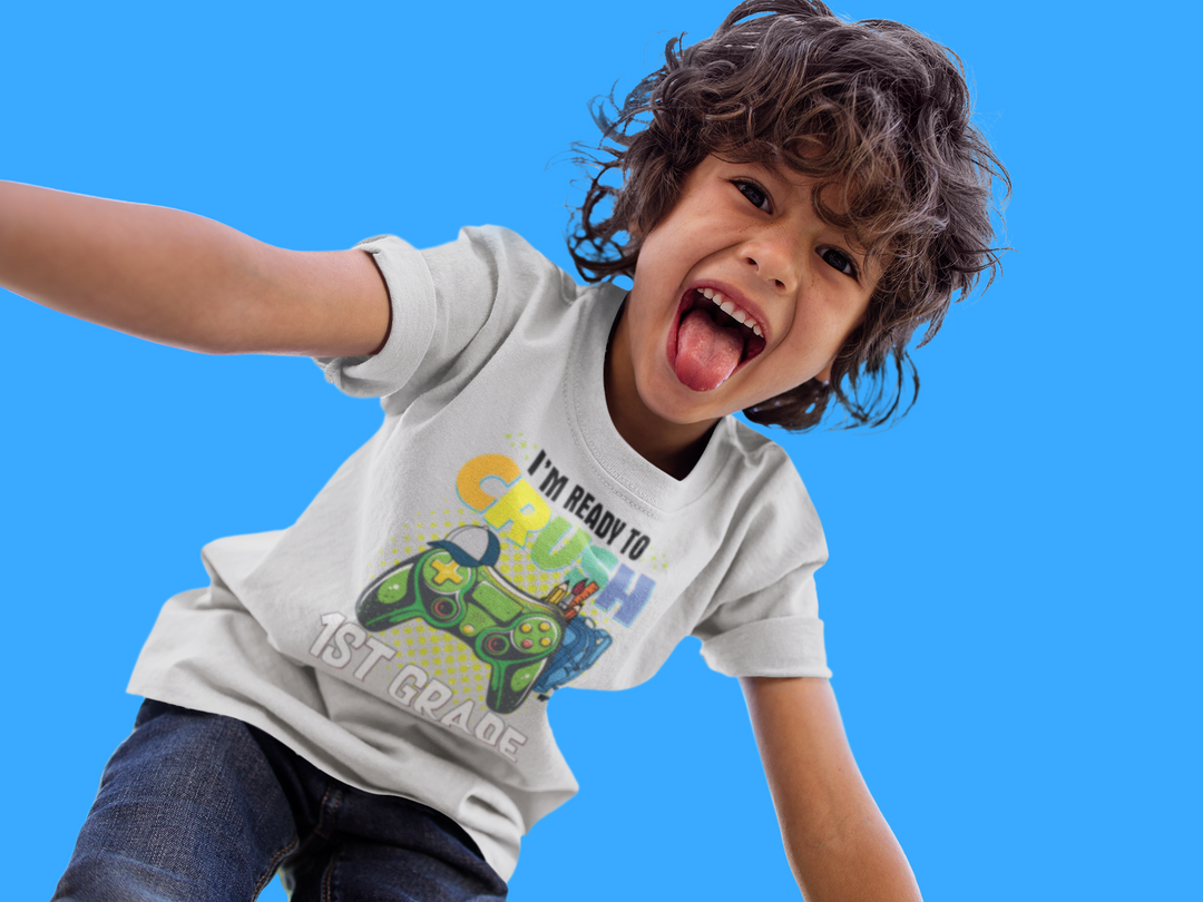 Child in white tee with cartoon sticking tongue out, ready to crush 1st grade. 100% cotton, light fabric, tear-away label, classic fit. Ideal for printing, durable twill tape shoulders, curl-resistant collar.