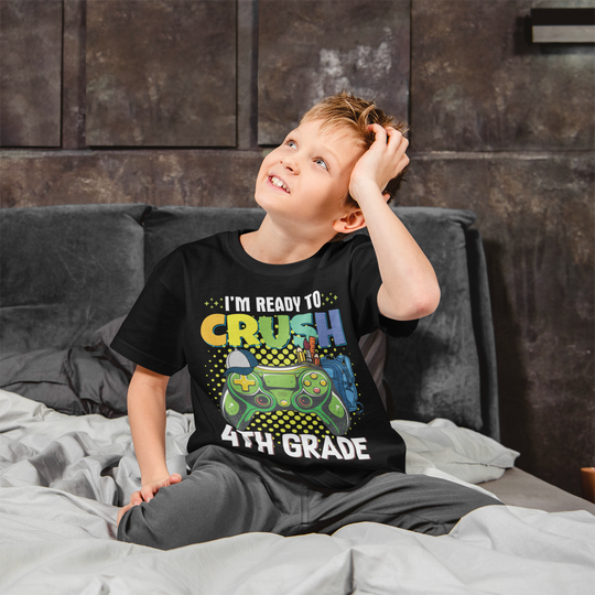 A boy in a black shirt sits on a bed, hand on head. Product: I'm Ready to Crush 4th Grade Kids Tee - 100% cotton, light fabric, tear-away label, classic fit. Ideal for everyday wear.