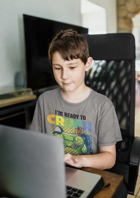 A boy in a grey shirt sits using a laptop, showcasing the I'm Ready to Crush 5th Grade kids tee. Classic fit, 100% cotton, tear-away label, ideal for everyday wear.