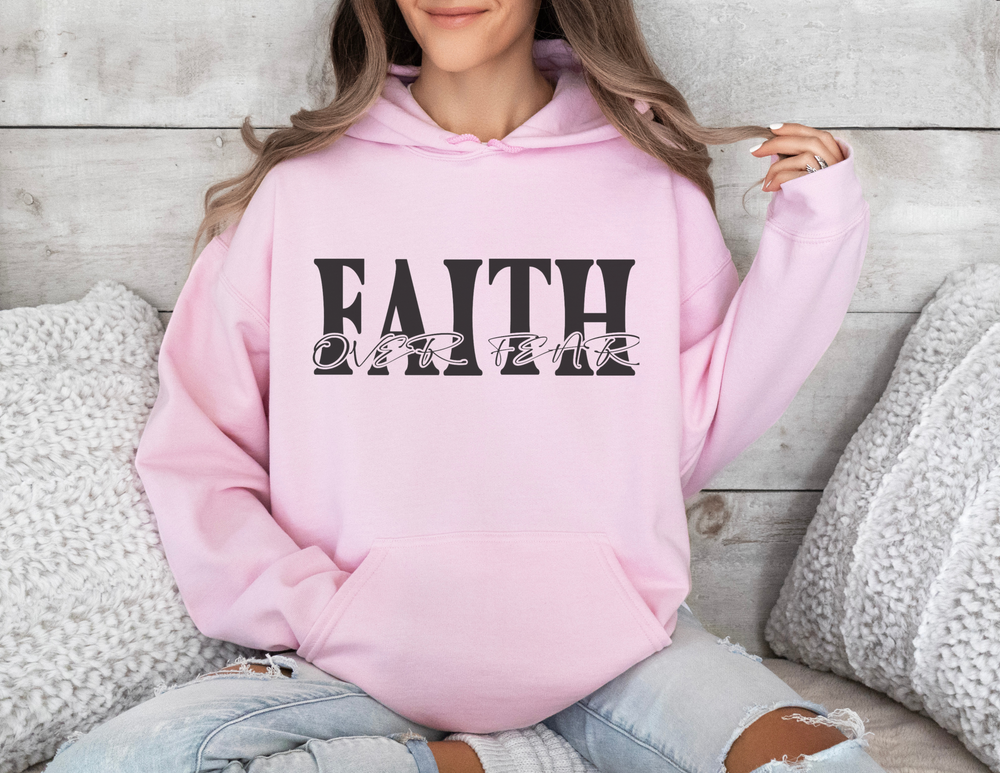 A woman in a cozy Faith Over Fear Hoodie, sitting on a couch. This unisex heavy blend hooded sweatshirt offers plush comfort with a kangaroo pocket and color-matching drawstring. Perfect for chilly days.