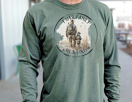 A man in a green Faith Family Hunting Long Sleeve T-Shirt, walking in a field with a child. Made of 100% ring-spun cotton for softness and style. Classic fit, garment-dyed fabric for comfort.