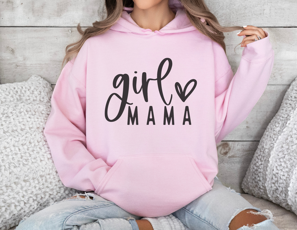 A woman in a pink Girl Mama Hoodie, sitting on a couch. Unisex heavy blend hooded sweatshirt made of cotton and polyester, cozy for cold days, with kangaroo pocket and matching drawstring.