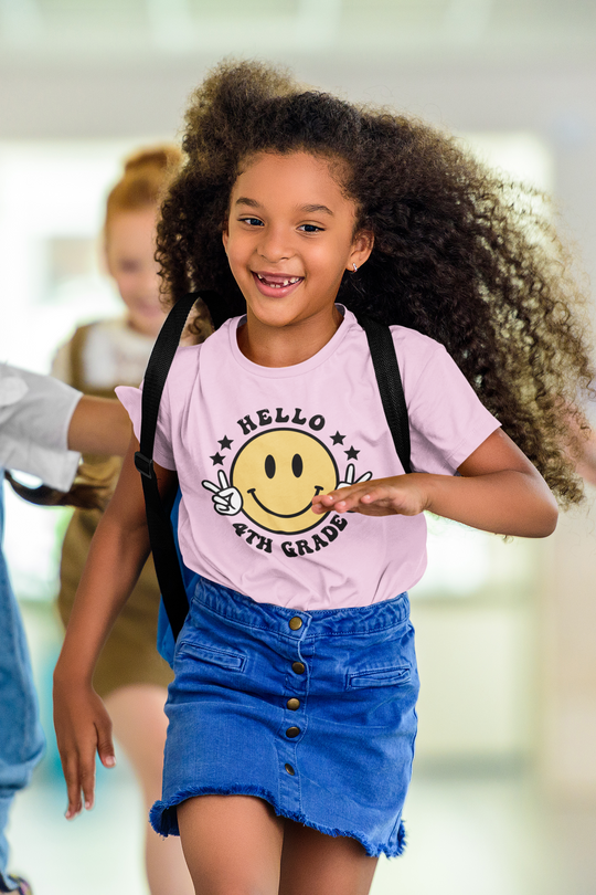 A girl with long curly hair running in a Hello 4th Grade Kids Tee, a 100% cotton tee perfect for everyday wear. Features twill tape shoulders and ribbed collar for durability. Classic fit, tear-away label.
