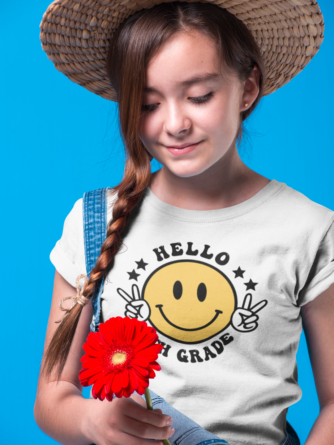 A girl in a straw hat holding a flower, showcasing the Hello 5th Grade Kids Tee. 100% cotton, light fabric, classic fit, tear-away label, durable twill tape shoulders, and ribbed collar. No side seams.