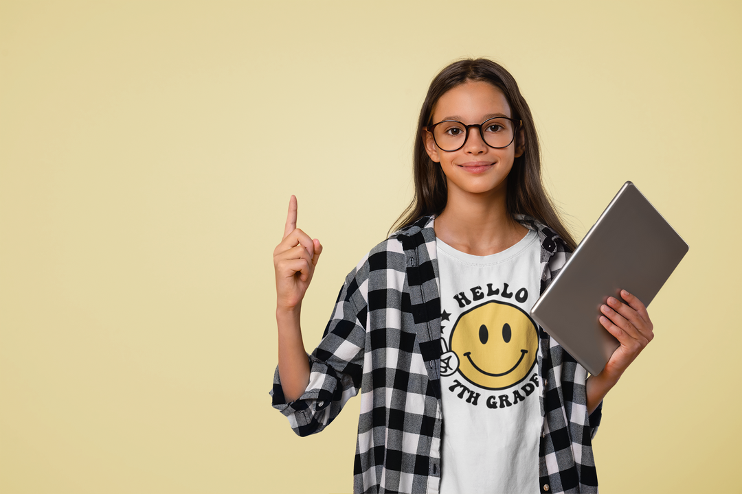 A premium fitted men’s short sleeve tee, Hello 7th Grade, featuring a girl holding a tablet and pointing up. Combed cotton, light fabric, ribbed knit collar, roomy fit. Ideal for workouts and daily wear.