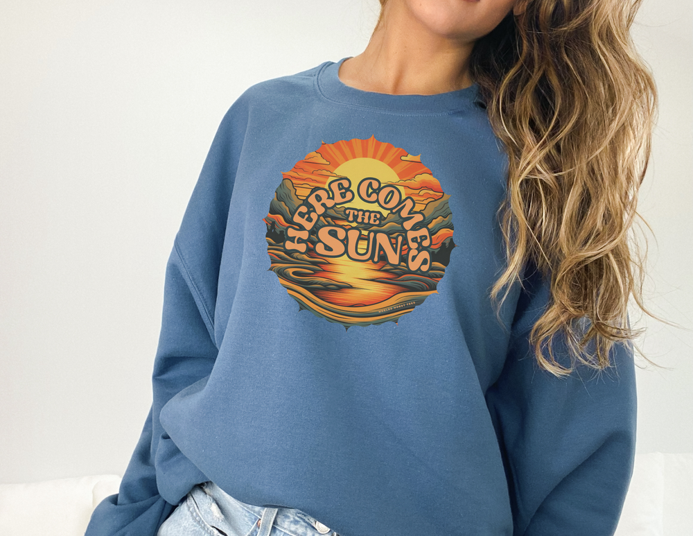 A woman in a blue crewneck sweatshirt, showcasing a comfortable fit. Unisex Here Comes the Sun Crew made of 50% Cotton 50% Polyester blend. Ribbed knit collar, no itchy side seams. Sizes from S to 5XL.