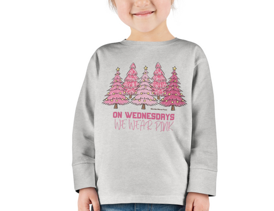 A smiling girl in a pink Christmas Toddler Long Sleeve Tee, showcasing a person in a sweatshirt. Made of 100% combed ringspun cotton, with ribbed collar and EasyTear™ label for comfort and durability.