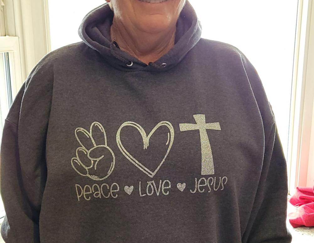 A unisex heavy blend hooded sweatshirt featuring Peace Love and Jesus design. Plush cotton-polyester fabric, kangaroo pocket, and drawstring hood. Classic fit, tear-away label, ideal for printing. From Worlds Worst Tees.