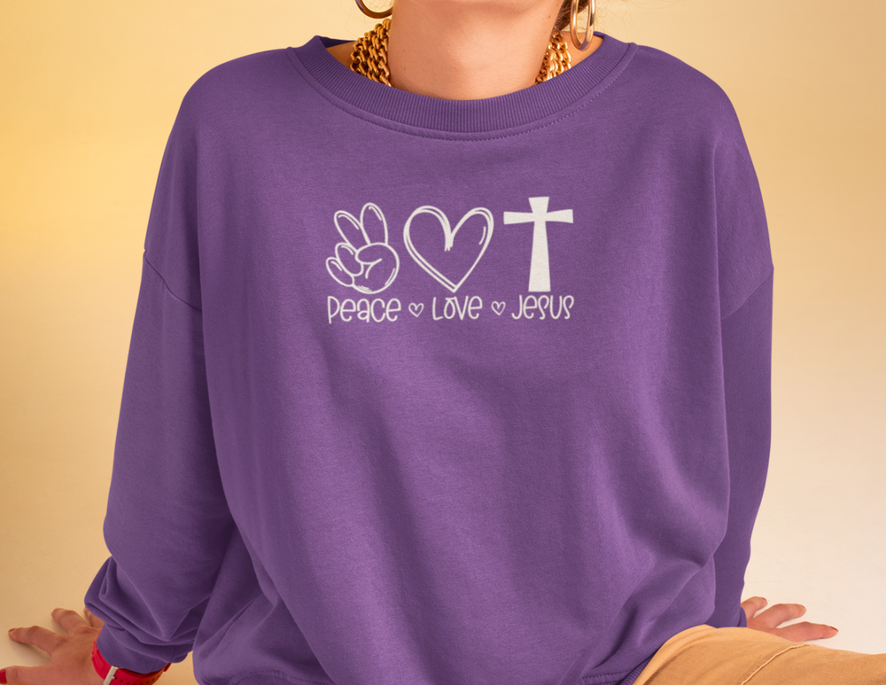 A cozy unisex heavy blend sweatshirt featuring Peace, Love, Jesus on a purple fabric. Classic fit, cotton-polyester blend, tear-away label. Perfect for cold days. From Worlds Worst Tees.