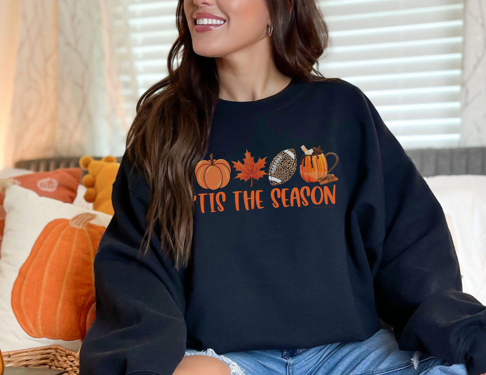 A woman on a couch smiles, showcasing the Tis the Season Crew sweatshirt. Unisex heavy blend, 50% cotton, 50% polyester, loose fit, ribbed knit collar, no itchy seams. Ideal comfort for any occasion.