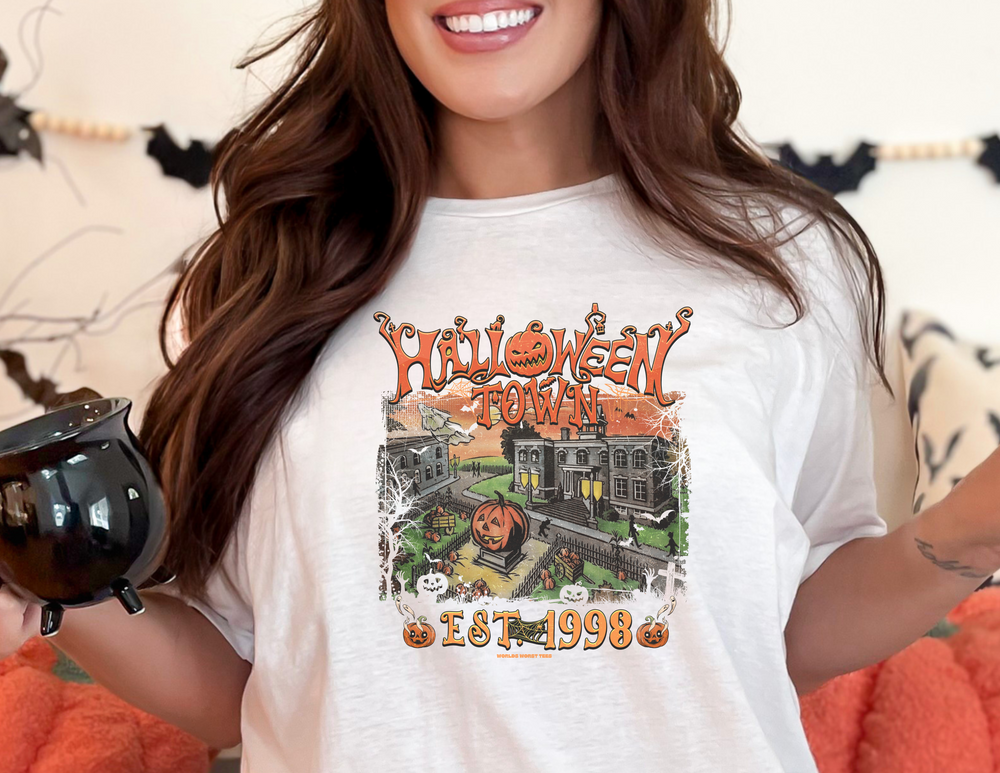 A woman in a Halloweentown Tee, smiling at the camera. Unisex garment-dyed sweatshirt, 80% ring-spun cotton, 20% polyester, relaxed fit, rolled-forward shoulder. From Worlds Worst Tees.