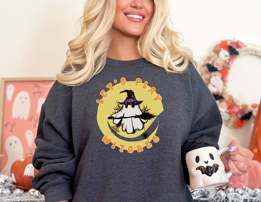Woman in Let's Play Witches Crew sweatshirt holding ghost mug, featuring cartoon ghost design. Made of 50% polyester and 50% USA cotton NuBlend® fleece. Size range from S to 3XL.