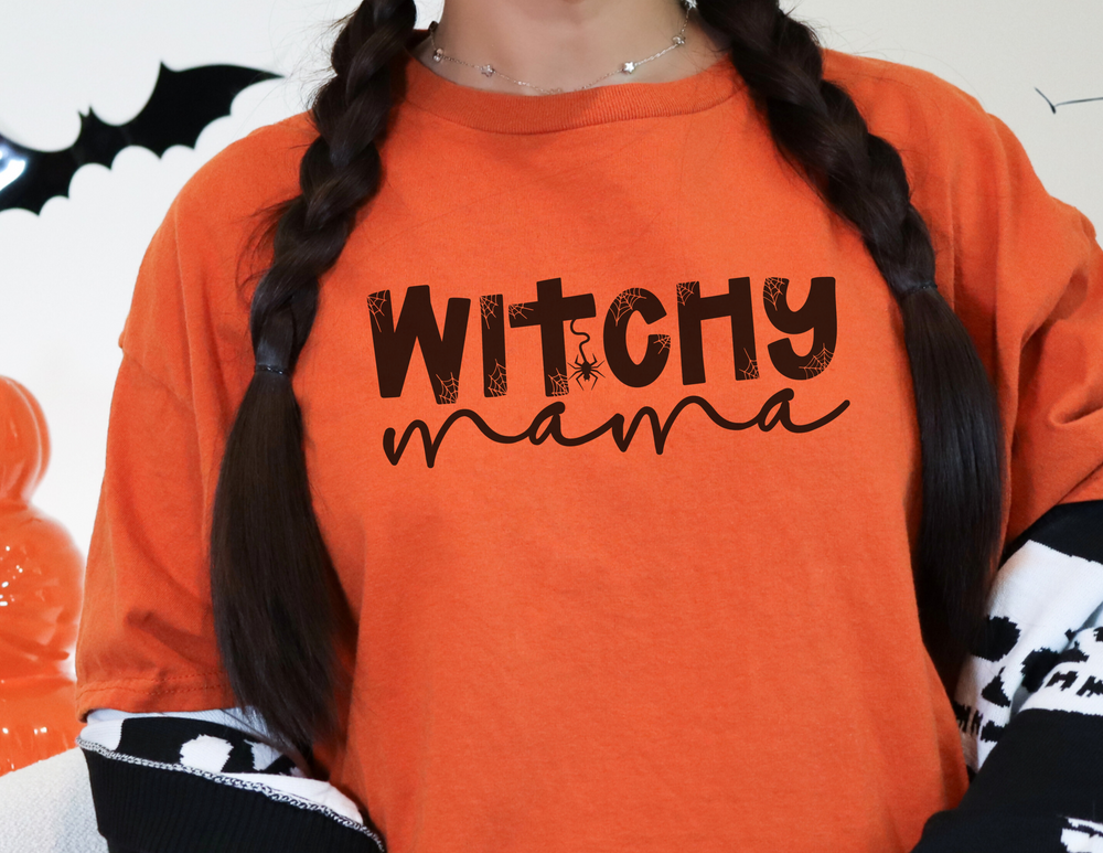 A woman in an orange Witchy Mama crewneck sweatshirt with braids, showcasing a loose fit, ribbed knit collar, and polyester-cotton blend for ultimate comfort. Ideal for any occasion.