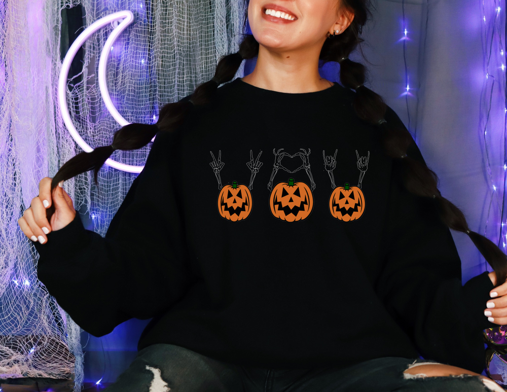 A woman in a Pumpkin Peace Love and Rock & Roll crewneck sweatshirt with pumpkins, smiling. Unisex heavy blend, loose fit, ribbed knit collar, polyester-cotton blend. Sizes S-5XL.