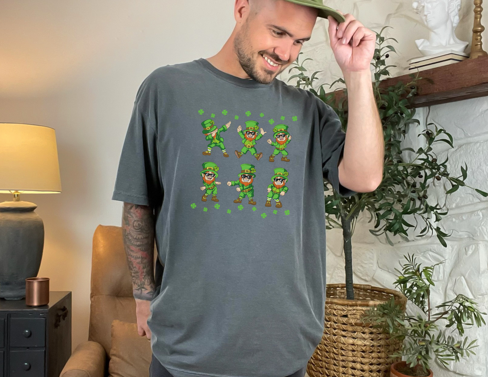 A man wearing a Dancing Leprechaun Tee, showcasing a grey shirt with green leprechauns. Unisex heavy cotton tee with ribbed knit collar, tape shoulders, and no side seams for comfort and durability. Classic fit, 100% cotton.