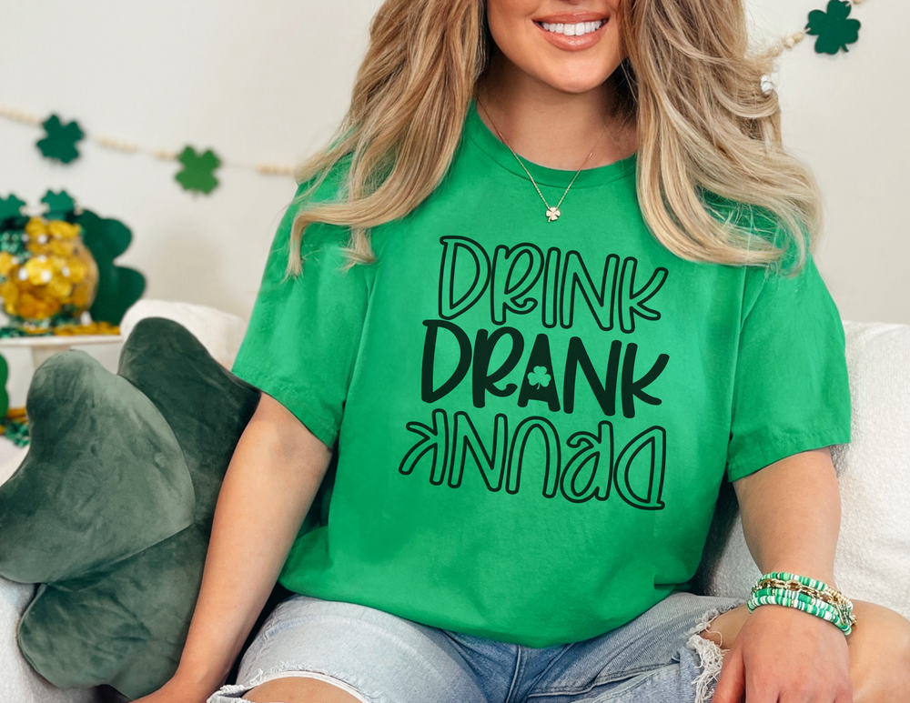 A woman in a green shirt smiles, showcasing the Drink-Drank-Drunk Unisex Tee. Classic fit, ribbed collar, and durable tape on shoulders. Ideal staple for casual fashion from Worlds Worst Tees.