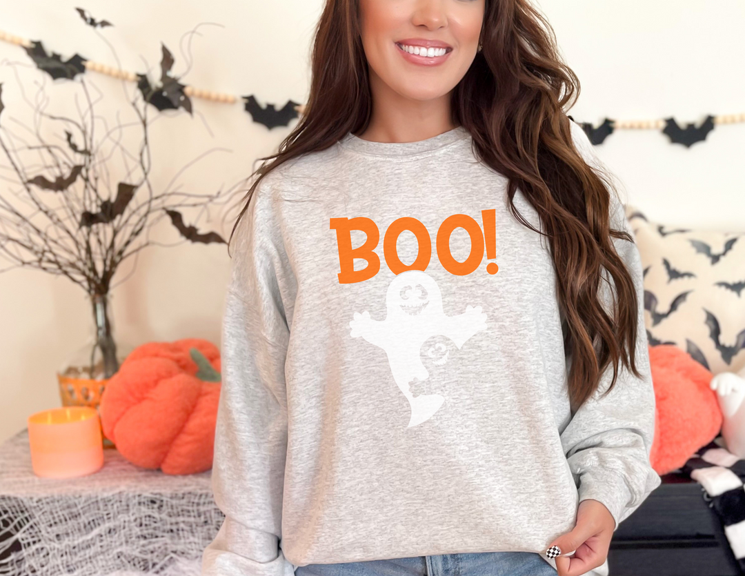 A woman in a grey sweater with orange text smiles at the camera, showcasing the Boo Crewneck sweatshirt from Worlds Worst Tees. Comfortable unisex blend with ribbed knit collar, ideal for any occasion.