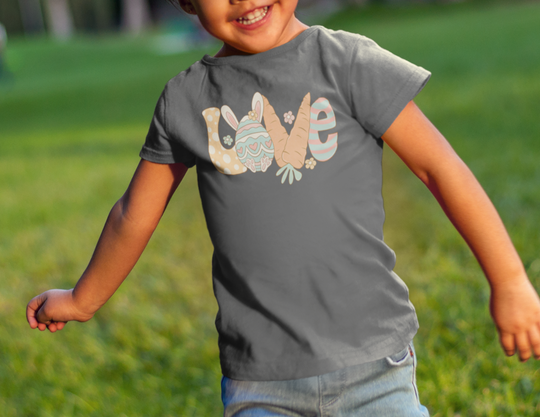 Love Easter Toddler Tee: A child in a grey shirt running in the grass, showcasing a classic fit with durable double-needle stitching. Made of 100% Ringspun cotton, light fabric, perfect for active kids.