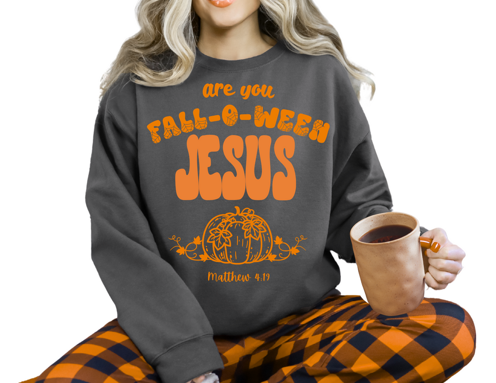 Person wears FALL-O-WEEN Jesus Crew sweatshirt with orange lettering and pumpkin, paired with plaid pants. Holds a mug, showcasing playful fall-themed outfit.