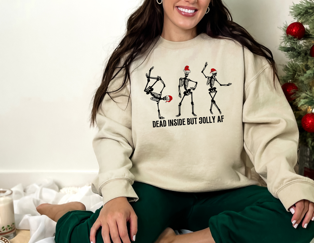 A woman in a Dead Inside But Jolly AF Crewneck sweatshirt, sitting on a bed surrounded by Christmas decorations. NuBlend® fleece, 50% polyester, 50% USA cotton, medium-heavy fabric, regular fit.