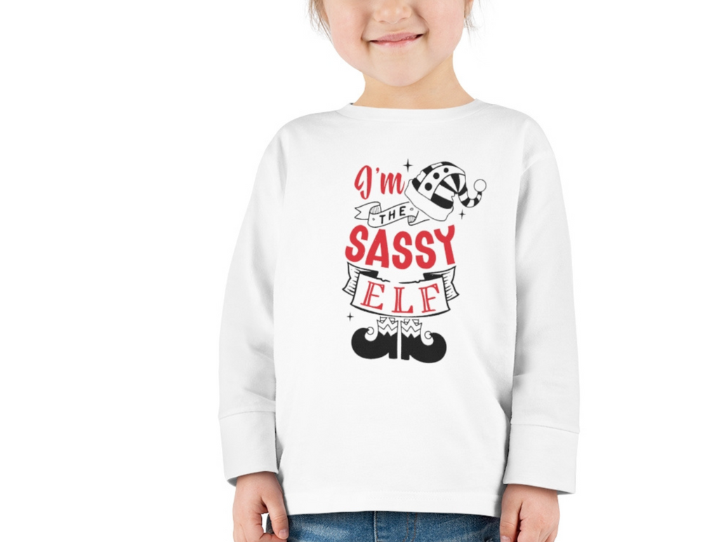 A toddler's long sleeve tee, I'm the Sassy Elf, in 100% Airlume cotton. Playful red text on white, with a smiling child. From Worlds Worst Tees.