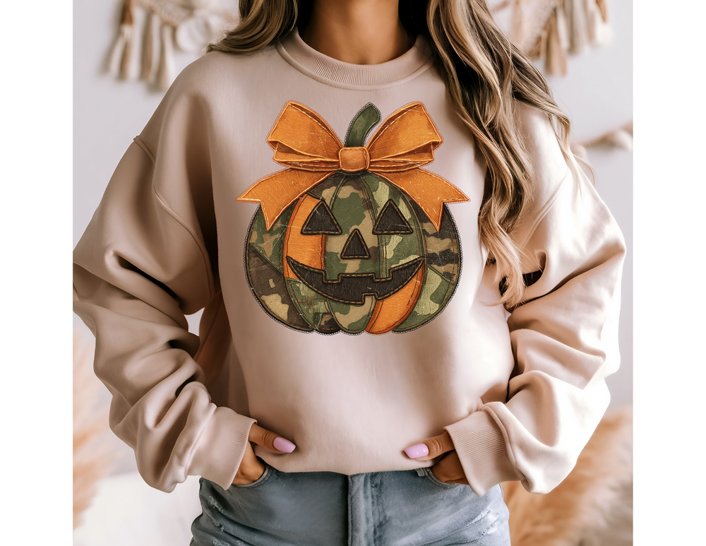 Person wearing a Jackie O Crew sweatshirt with a camouflage jack-o-lantern graphic and orange bow, paired with light-wash jeans, showcasing cozy seasonal style.