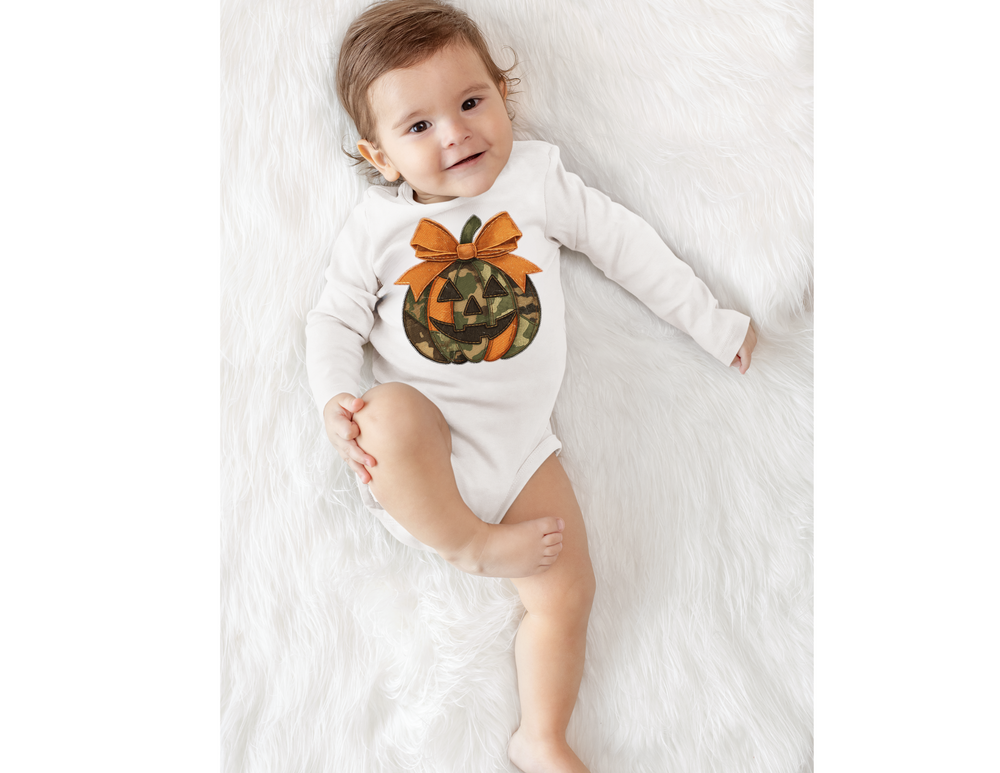 Baby wearing Jackie O Long Sleeve Onesie with camo jack-o’-lantern print, lying on a fluffy rug, smiling, showcasing soft, durable fabric and easy-change snaps.