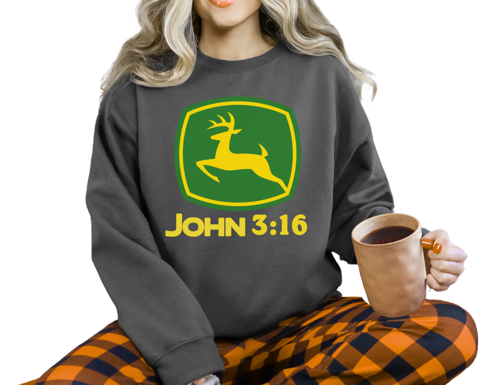 Person wearing a John 3:16 Crew dark-gray sweatshirt with a deer emblem and plaid pants, holding a large mug, seated cross-legged.
