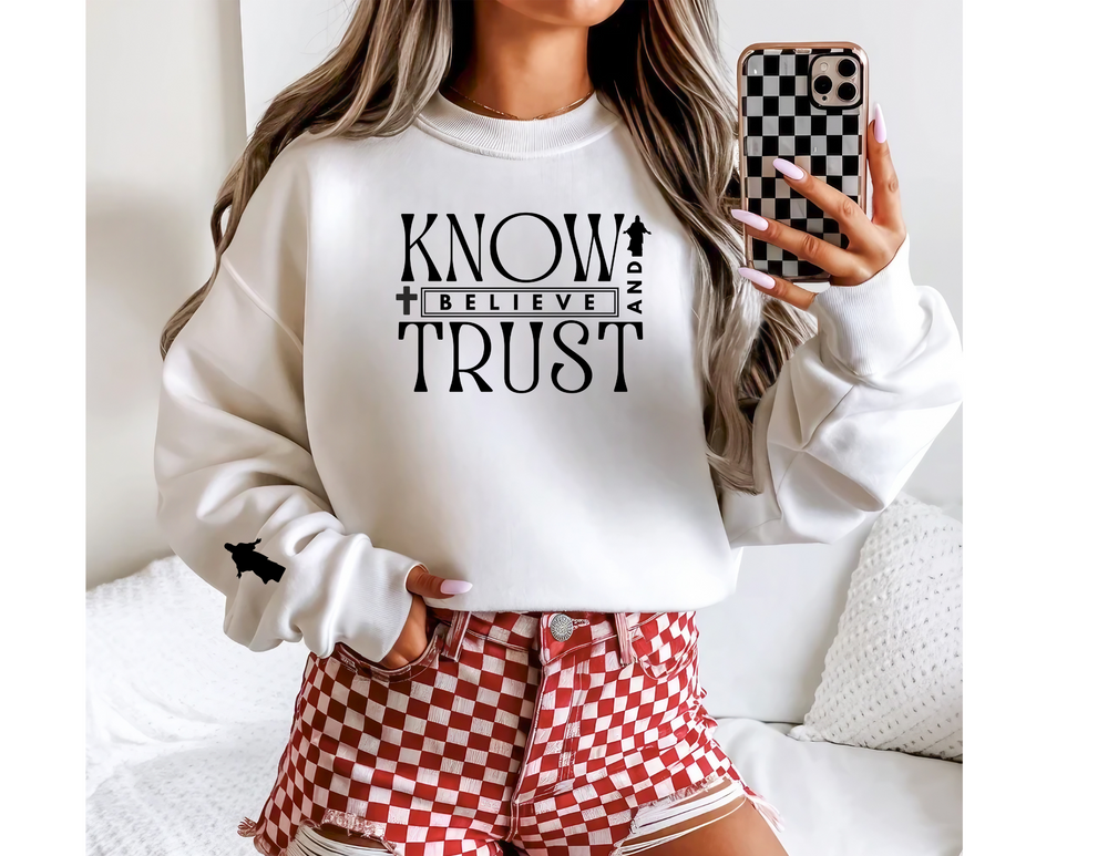 Woman wearing Trust, Know, Believe Crew sweatshirt, showcasing its casual, comfortable design with a ribbed collar and checkered shorts, ideal for colder months.