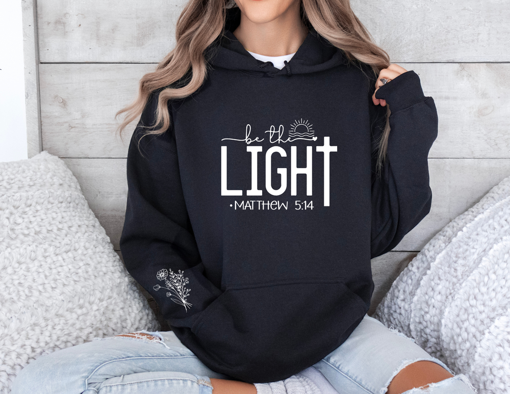 A unisex Be the Light Hoodie, a cozy blend of cotton and polyester, featuring a kangaroo pocket and matching drawstring hood. Medium-heavy fabric for warmth and comfort. Perfect for chilly days.