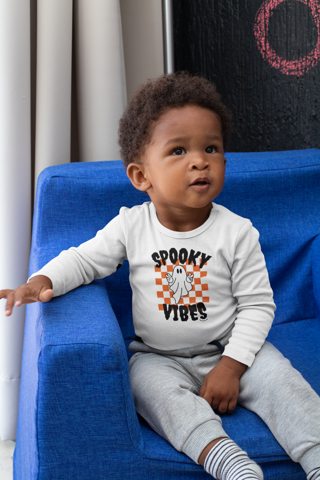 A spooky vibes long-sleeved onesie for infants, featuring a ghost design on a blue chair. Made of soft, durable fabric with plastic snaps for easy changing. Ideal for baby's comfort and style.