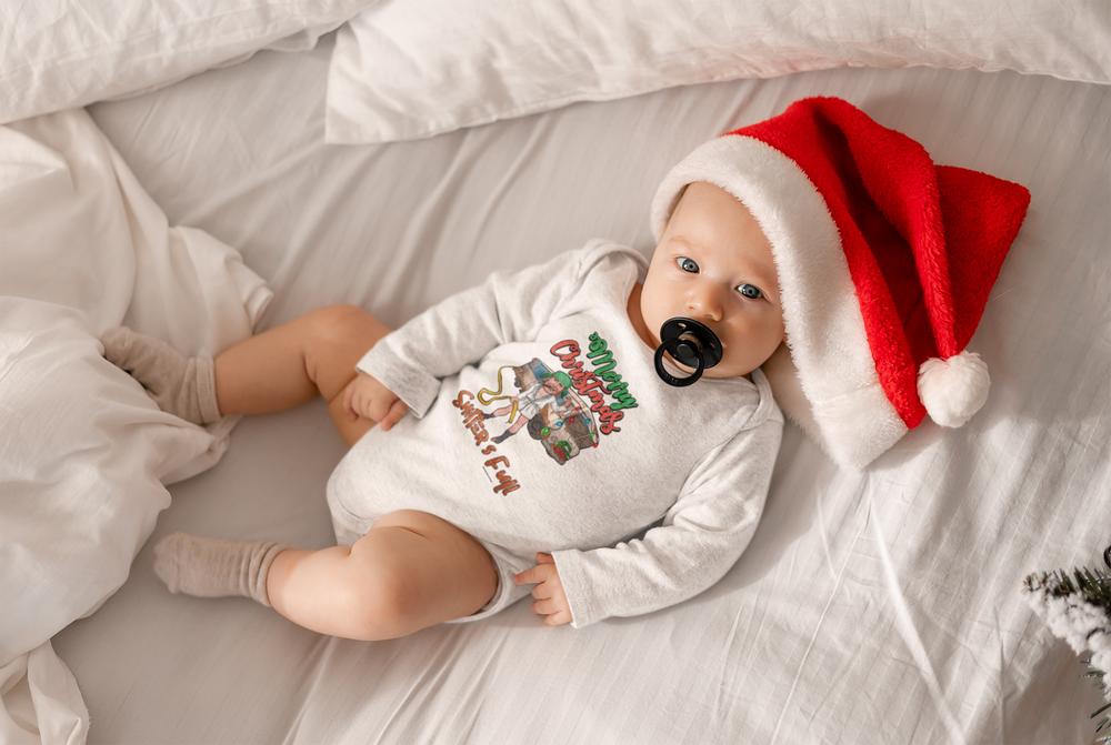 A baby wearing a Santa hat lies on a bed, showcasing the Shitter's Full Onesie from Worlds Worst Tees. This infant long sleeve bodysuit features soft cotton fabric and convenient plastic snaps for easy changing.