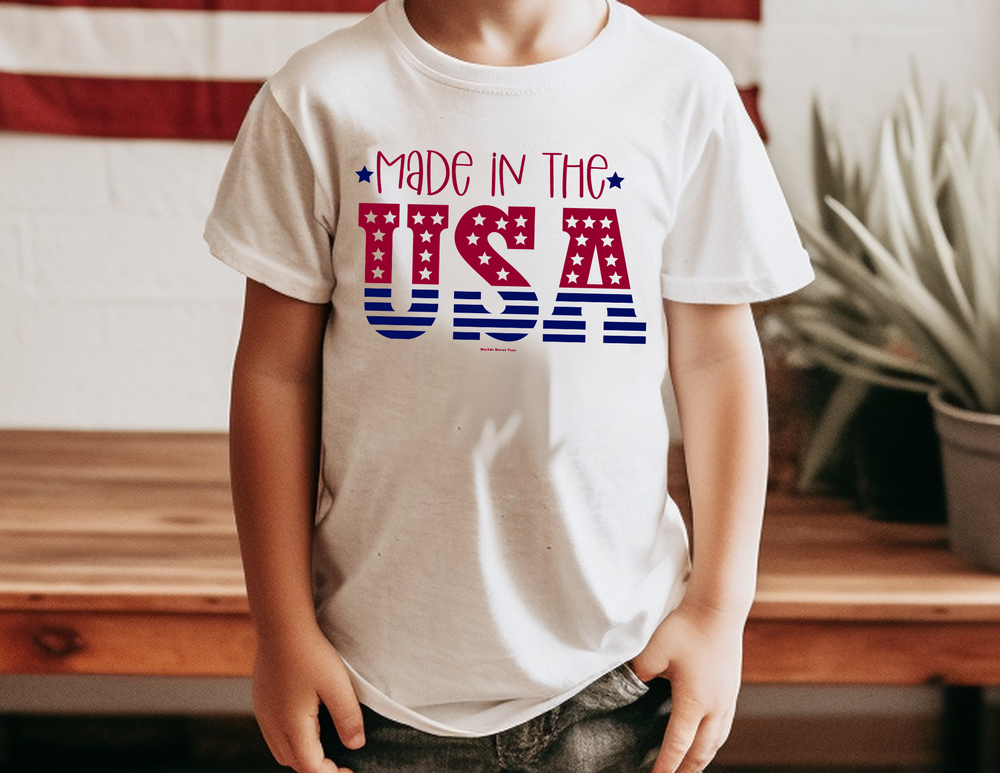 A Made in the USA Toddler Tee featuring a boy in a white shirt with red and blue text. Soft 100% combed ringspun cotton, tear-away label, classic fit. Sizes: 2T, 3T, 4T, 5-6T.