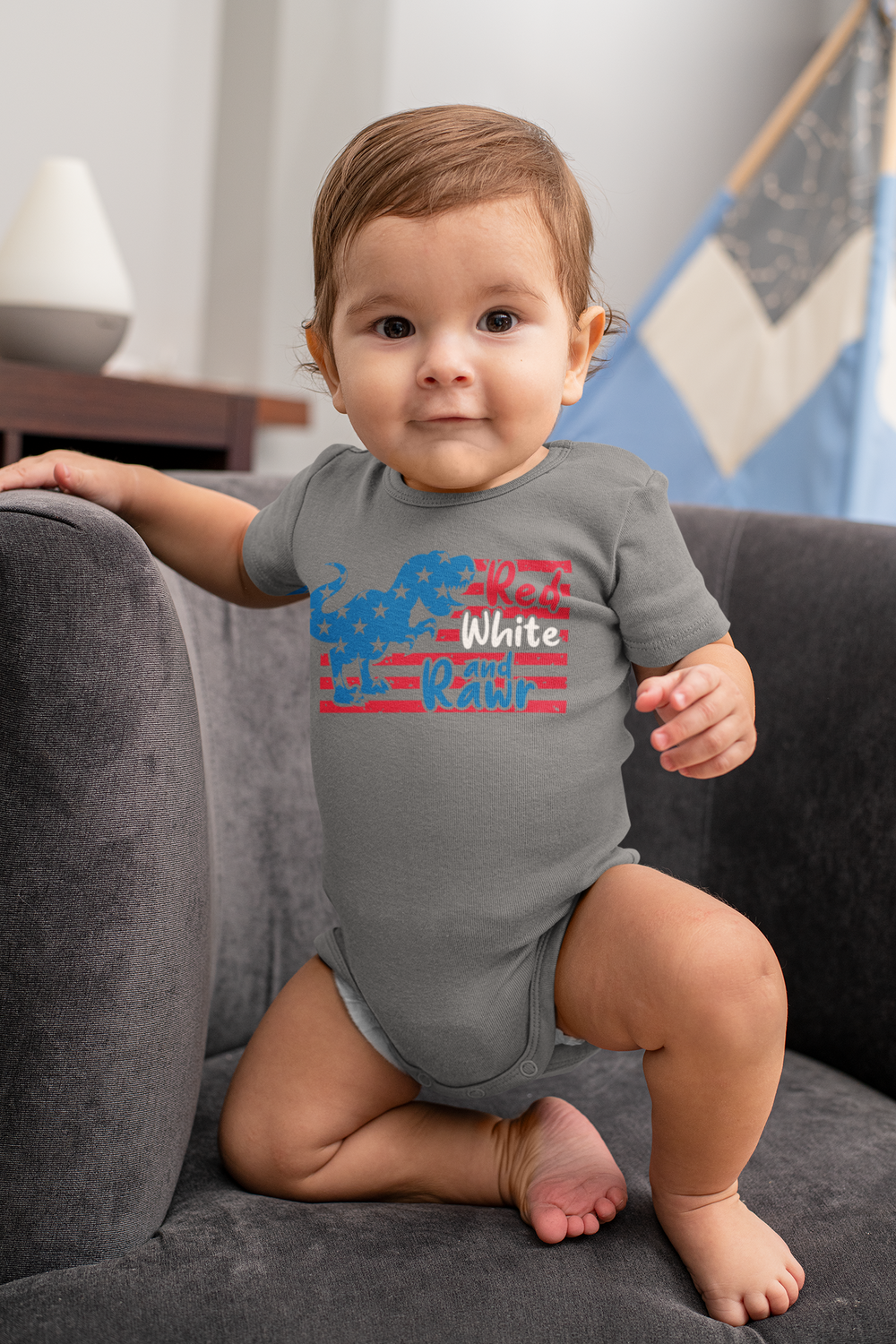 A baby in a Red White and Rawr onesie, sitting on a chair. Infant fine jersey bodysuit made of 100% cotton, featuring ribbed knitting for durability and plastic snaps for easy changing access. Combed ringspun cotton, light fabric.