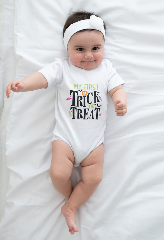 A Trick or Treat Onesie for babies, featuring a baby lying on a white blanket. Made of 100% cotton, with ribbed bindings and plastic snaps for easy changing. Infant fine jersey bodysuit in various sizes.