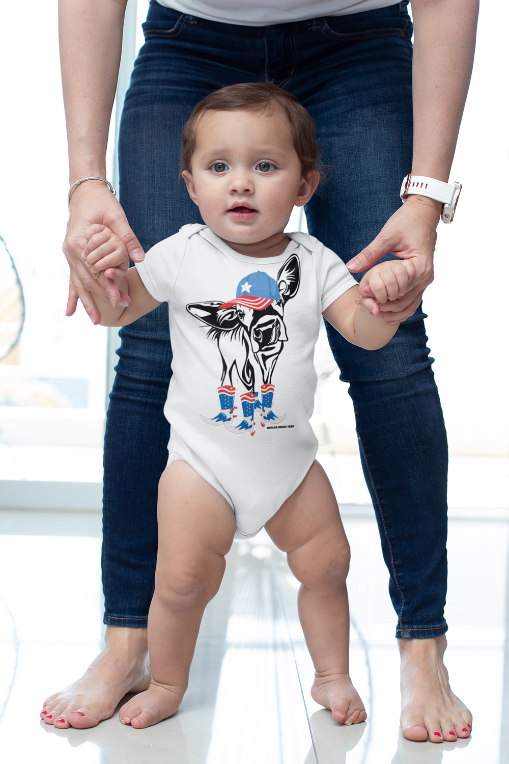A baby wearing a white onesie featuring a cow design, with a person's hands supporting the baby. This infant fine jersey bodysuit is 100% cotton, with ribbed knitting for durability and plastic snaps for easy changes. From Worlds Worst Tees.