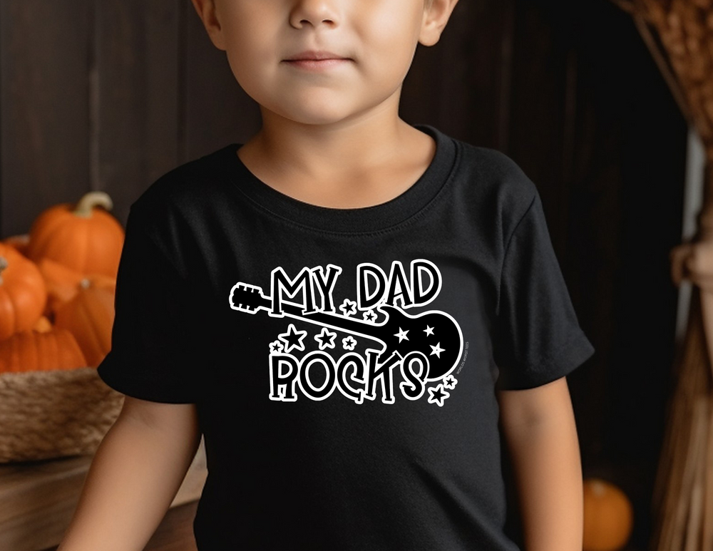 A toddler wearing a black My Dad Rocks tee, perfect for sensitive skin. Made of 100% combed ringspun cotton, light fabric, with a classic fit. Ideal for first ventures.