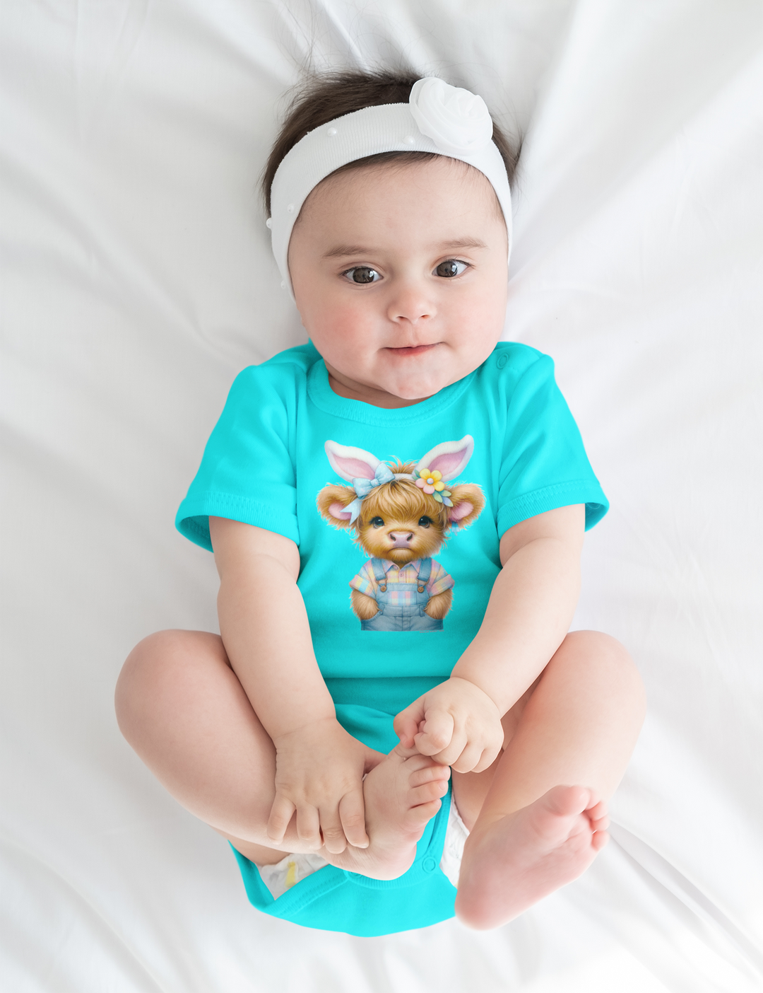 A baby wearing an Easter Cow Onesie, lying on a white sheet. Infant fine jersey bodysuit made of 100% cotton, featuring ribbed knitting for durability and plastic snaps for easy changing access.