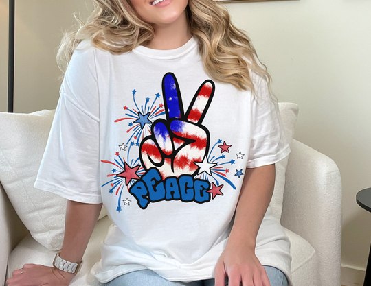 A woman in a white Peace America Tee, sitting on a chair, showcasing a classic fit unisex heavy cotton tee. No side seams, durable shoulders, and ribbed knit collar. Medium weight fabric.