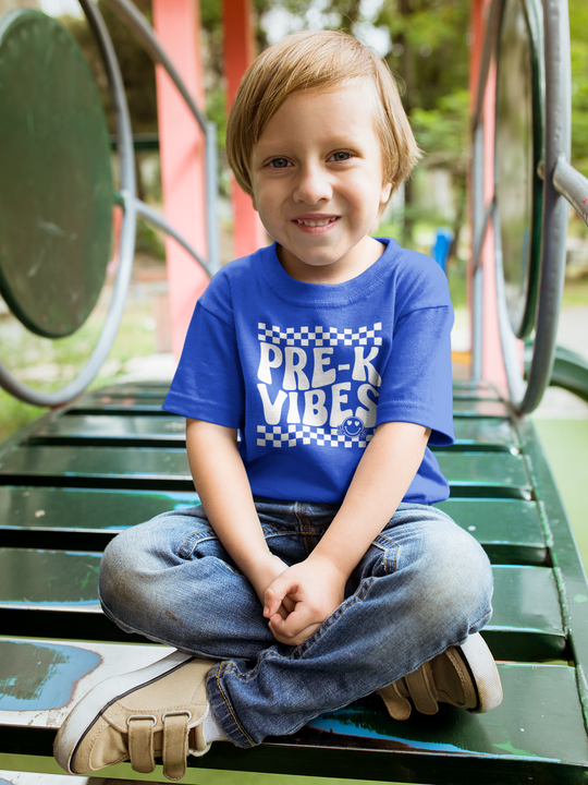 A Pre K Vibes Toddler Tee featuring a child on a playground slide, smiling at the camera. Made of 100% combed ringspun cotton, light fabric, tear-away label, and a classic fit. Ideal for sensitive skin.