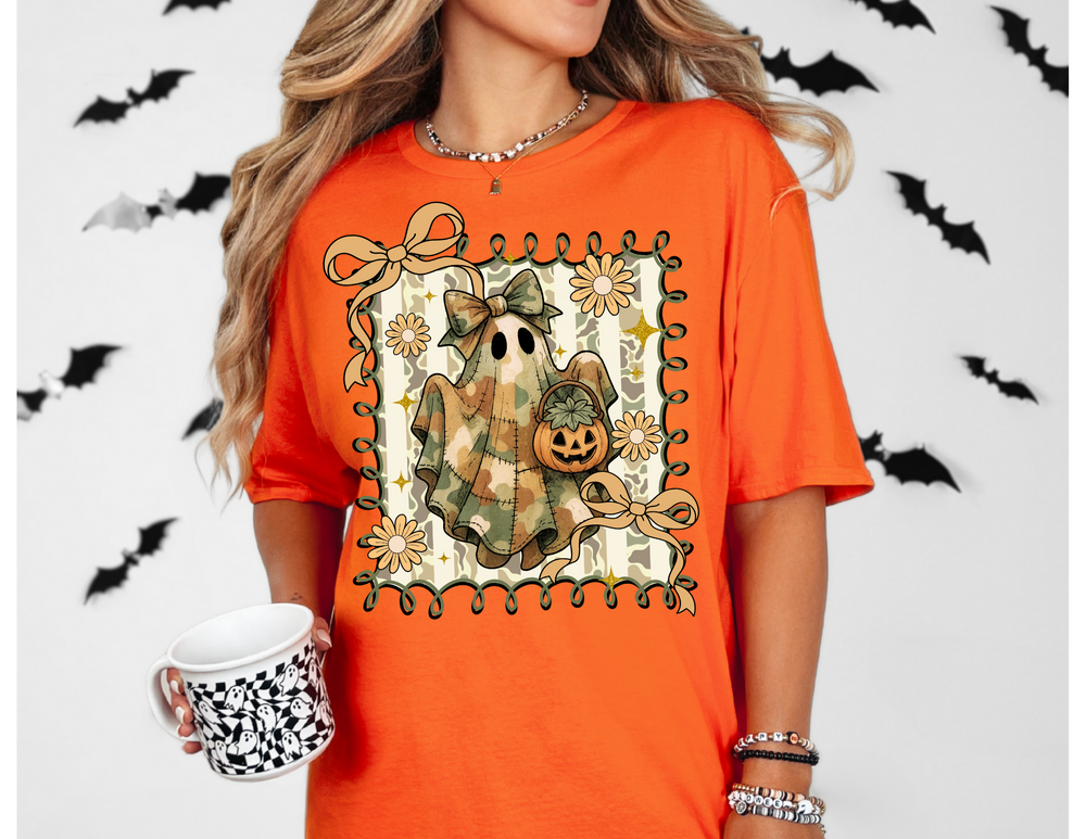 Quilted Ghost Tee features a camo-patterned ghost with a bow, jack-o’-lantern, and vine border, perfect for adding whimsy to your Halloween wardrobe.