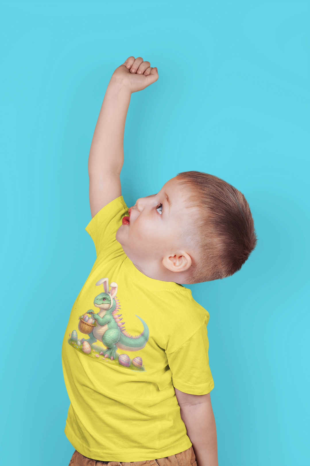 A child in a dinosaur tee raises his hand, showcasing the Eggosaurus Toddler Tee from Worlds Worst Tees. Soft, 100% cotton, with a durable print, perfect for sensitive skin. Sizes from 2T to 5-6T.