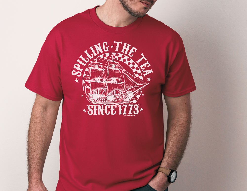 A man in a red shirt featuring the Spilling the Tea Since 1773 Tee design. Unisex jersey tee with ribbed knit collar, taping on shoulders, and 100% Airlume combed cotton. Soft, quality print for a retail fit.