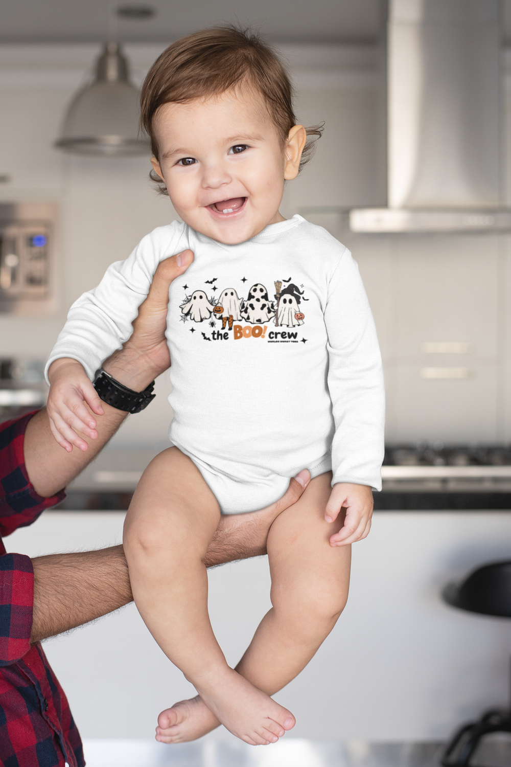 A baby in a white Boo Crew Long Sleeved Onesie, held by a man. Infant bodysuit with ribbed bindings for durability, soft cotton fabric, and plastic snaps for easy changing. Classic fit for comfort.