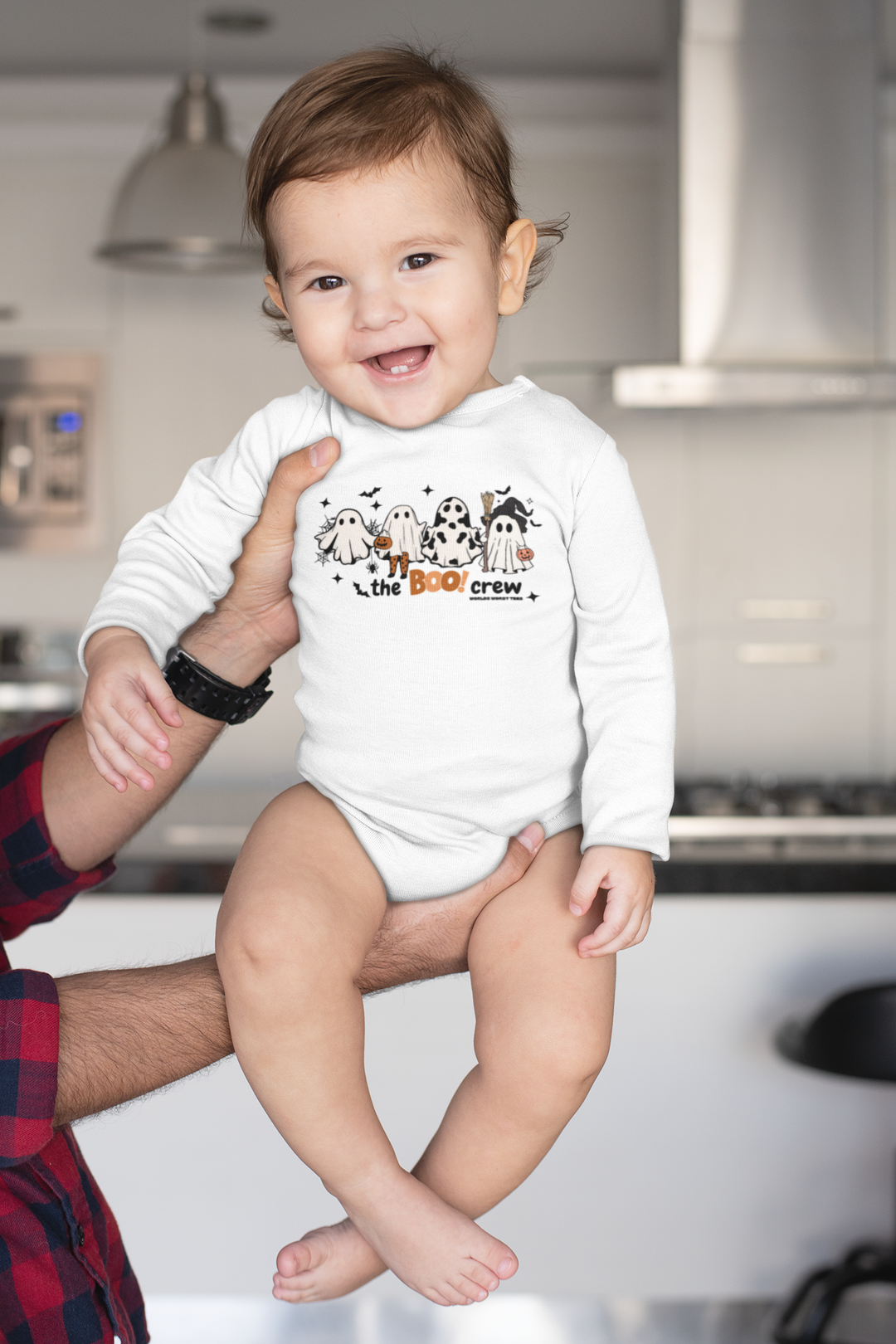 A baby in a white Boo Crew Long Sleeved Onesie, held by a man. Infant bodysuit with ribbed bindings for durability, soft cotton fabric, and plastic snaps for easy changing. Classic fit for comfort.